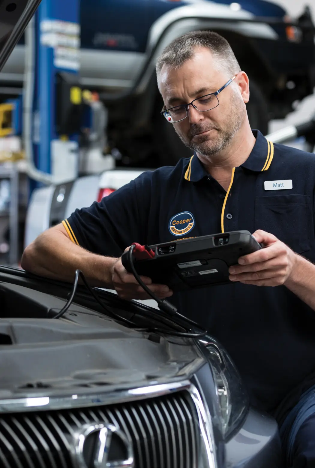 Cooper Automotive Mechanic standing beside a vehicle and holding a device